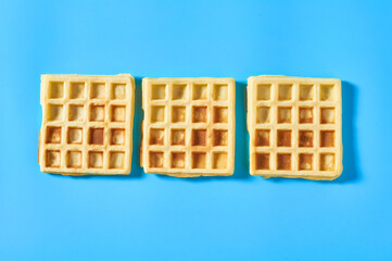 Row of three vanilla belgian waffles on blue background