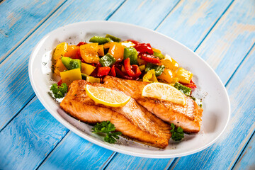 Fried salmon steaks with lemon and bell pepper served on wooden table
