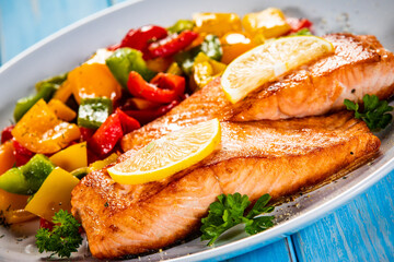 Fried salmon steaks with lemon and bell pepper served on wooden table
