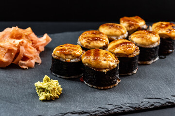 Served warm sushi rolled in nori sheets with ginger and wasabi on a black stone plate.