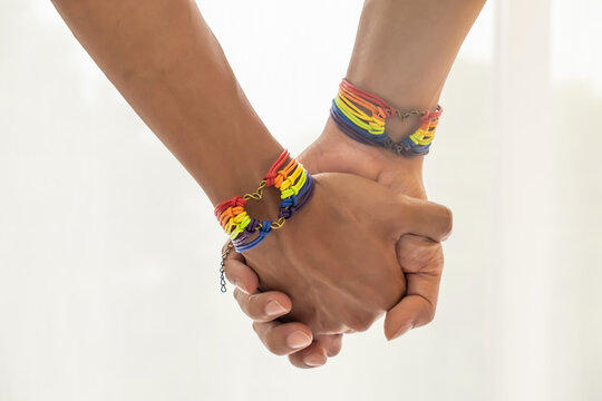 Close up shot of Asian Male couple holding hands with gay pride rainbow awareness wristbands. LGBT, same-sex love and homosexual relationships with copy space.
