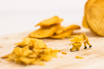Miniature people, Workers work on  production potato chips on white background (food concept)
