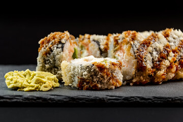 Served warm sushi with wasabi on a black stone plate.
