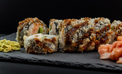 Served warm sushi with ginger and wasabi on a black stone plate.