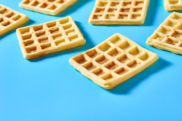 Scattered vanilla belgian waffles on blue background