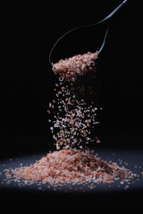 Spilling salt, from a black plastic spoon onto a wooden table. All on dark background