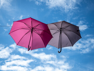 Fototapeta na wymiar Two decorative pink and grey umbrellas hanging on ropes in the air on blue sky background with clouds. Horizontal picture