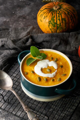 Traditional pumpkin soup puree with cream and seeds in a bowl, on a dark background