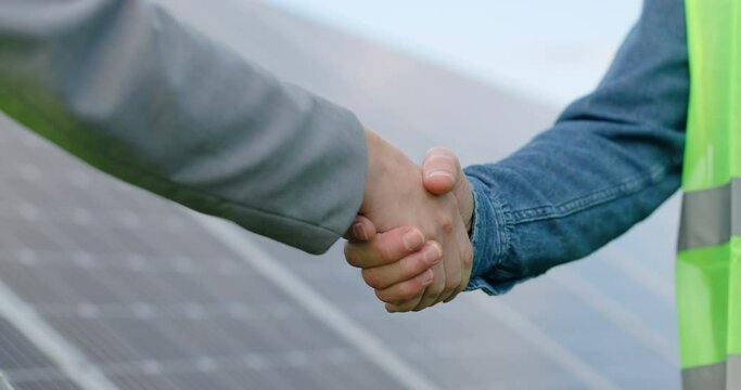 Close Up Of Handshake On Solar Panel Background Outside. Female Engineer Shakes Hands With Partner In Agreement.