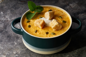 Traditional pumpkin soup puree with crackers, cream and seeds in a bowl, on a dark background