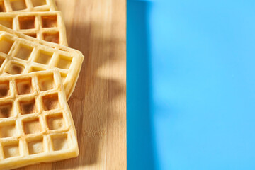 Vanilla belgian waffles on wooden cutting board on blue background