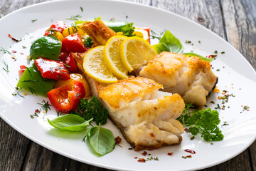 Fish dish - fried cod fillet with fried vegetables and lemon served on wooden table