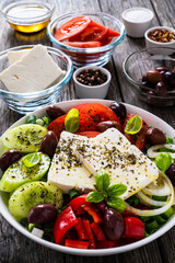 Fresh Greek salad - feta cheese, tomatoes, cucumber, red pepper, black olives and onion on wooden table
