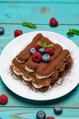 portion of Classic tiramisu dessert with raspberries and blueberries on blue wooden background