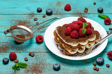portion of Classic tiramisu dessert with raspberries and blueberries on blue wooden background