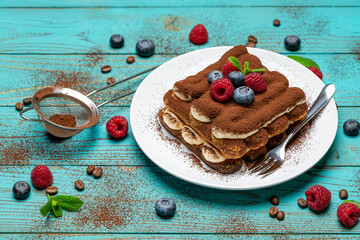 portion of Classic tiramisu dessert with raspberries and blueberries on blue wooden background