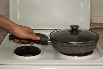 a man holds a frying pan by the handle, which stands on the hotplate of an electric stove