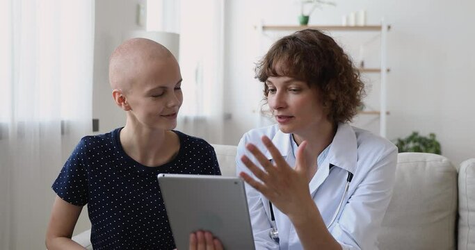 Cancer patient listen 40s doctor hold tablet showing chemo test health results. Oncologist practitioner encouraging ill girl during visit in clinic. Rehabilitation and forecasting of disease concept