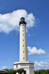 Fototapeta na wymiar Tall white lighthouse over a blue sky sorrunded by some clouds