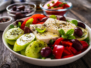 Fresh Greek salad - feta cheese, tomatoes, cucumber, red pepper, black olives and onion on wooden table
