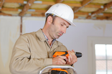 male technician holding power drill on ladder