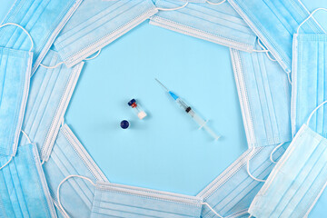 Syringe and jars with a vaccine in a frame of medical masks on a blue background.