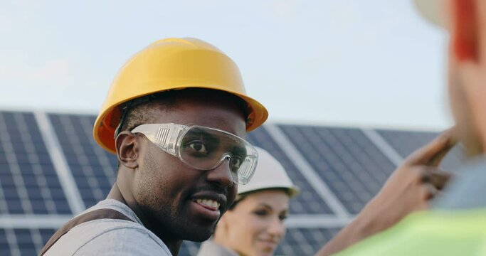 Close up portrait of young handsome african american man in hardhat and goggles walking talking about solar energy and batteries.