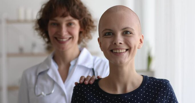 Middle-aged woman oncology nurse practitioner standing behind cancer patient, smile look at camera, head shot portrait. Doctor supporting ill girl put hand on shoulder as symbol of help and compassion