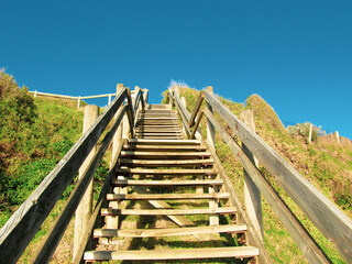 Ground view of wooden beach steps at Sandringham, VIC, Australia. The steps lead to a white sandy beach which is a popular location for beachgoers. This suburb is one of Melbourne's bayside suburbs.
