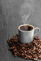 Black coffee in small cup with beans on black stone background