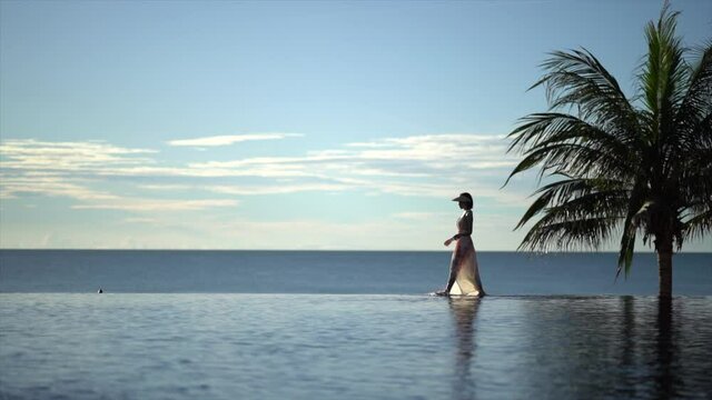 Woman walking on edge of infinity pool in the morning.