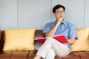 senior asian man reading a book on sofa