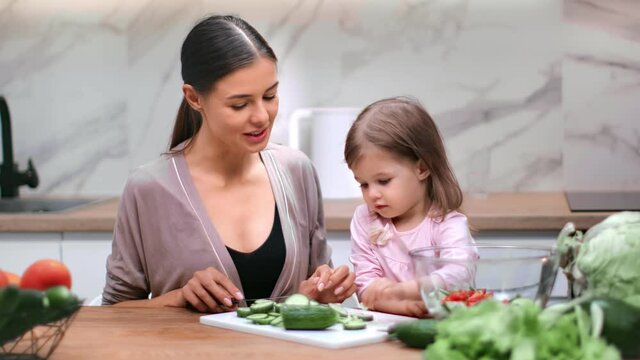 Mother and daughter cutting cucumber cooking vegetable salad together. Shot with RED camera in 4K