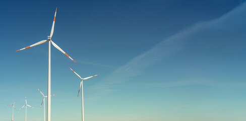 Banner with pair of big wind turbines to generate electrical power, green ecofriendly energy at blue sky with sunset warm colors with copy space for text. © neurobite