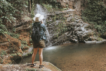 Woman tourist traveling adventure through the forest Successfully arrived at the destination until you reach the waterfall.wearing travel gear hat and camera.outdoor freedom lifestyle.