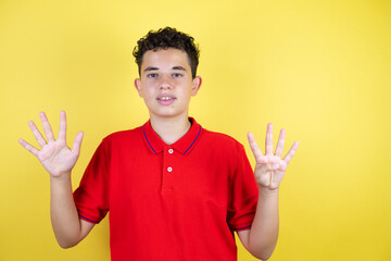 Beautiful teenager boy over isolated yellow background showing and pointing up with fingers number...