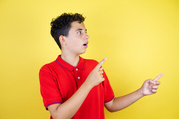 Beautiful teenager boy over isolated yellow background surprised, looking and pointing side