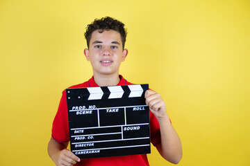 Beautiful teenager boy over isolated yellow background holding clapperboard very happy