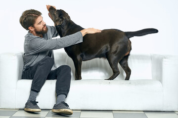 man with a black dog on a white sofa on a light background close-up cropped view pet human friend...