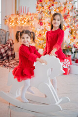 Two girls have fun riding toy horse in front of a Christmas tree