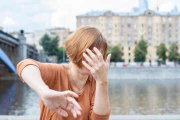 Frightened adult redhead woman in casual clothes extending her hand with open palm showing stop...