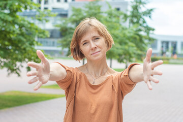 A joyful middle-aged redhead woman in casual clothes stands in the street with her arms...