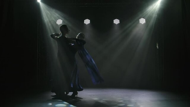 A silhouette of a couple who is dancing the classic ballroom dance waltz in a dark studio. Dancers in the spotlight. Slow motion.