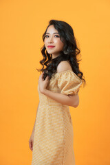 Portrait of a smiling attractive woman in summer dress posing while standing isolated over yellow background