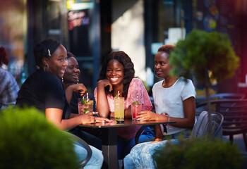 Happy African American Women, friends sitting together at the outdoor restaurant at summer day
