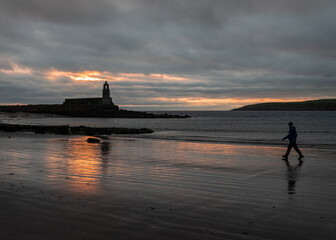 Silhouette of Harbour Light Tower and walker at dusk, Port Lagon, Dumfries & Galloway, Scotland.