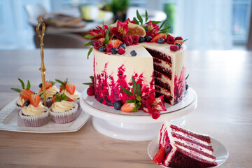 Big beautiful red velvet cake, with flowers and berries on top. Slice on a plate, dessert.