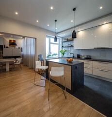Fototapeta premium Modern interior of kitchen in luxury apartment. White cabinets. Wooden kitchen set with sink. Table and chairs. Living room.