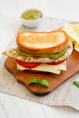 Homemade Pesto Chicken Sandwich with Potato Chips on a rustic wooden board on a white wooden table, low angle view.