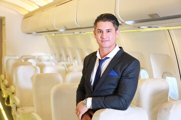 Handsome Caucasian businessman in formalwear inside the airplane with passenger seat on the background with copy space